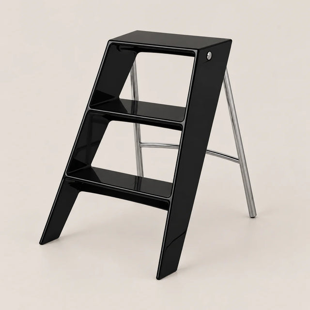 A modern black step stool with a glossy finish and silver metal support legs, shown on a clean, solid light beige background.