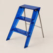 A three-step folding step ladder made of translucent blue plastic with silver metal legs, shown on a light beige background.