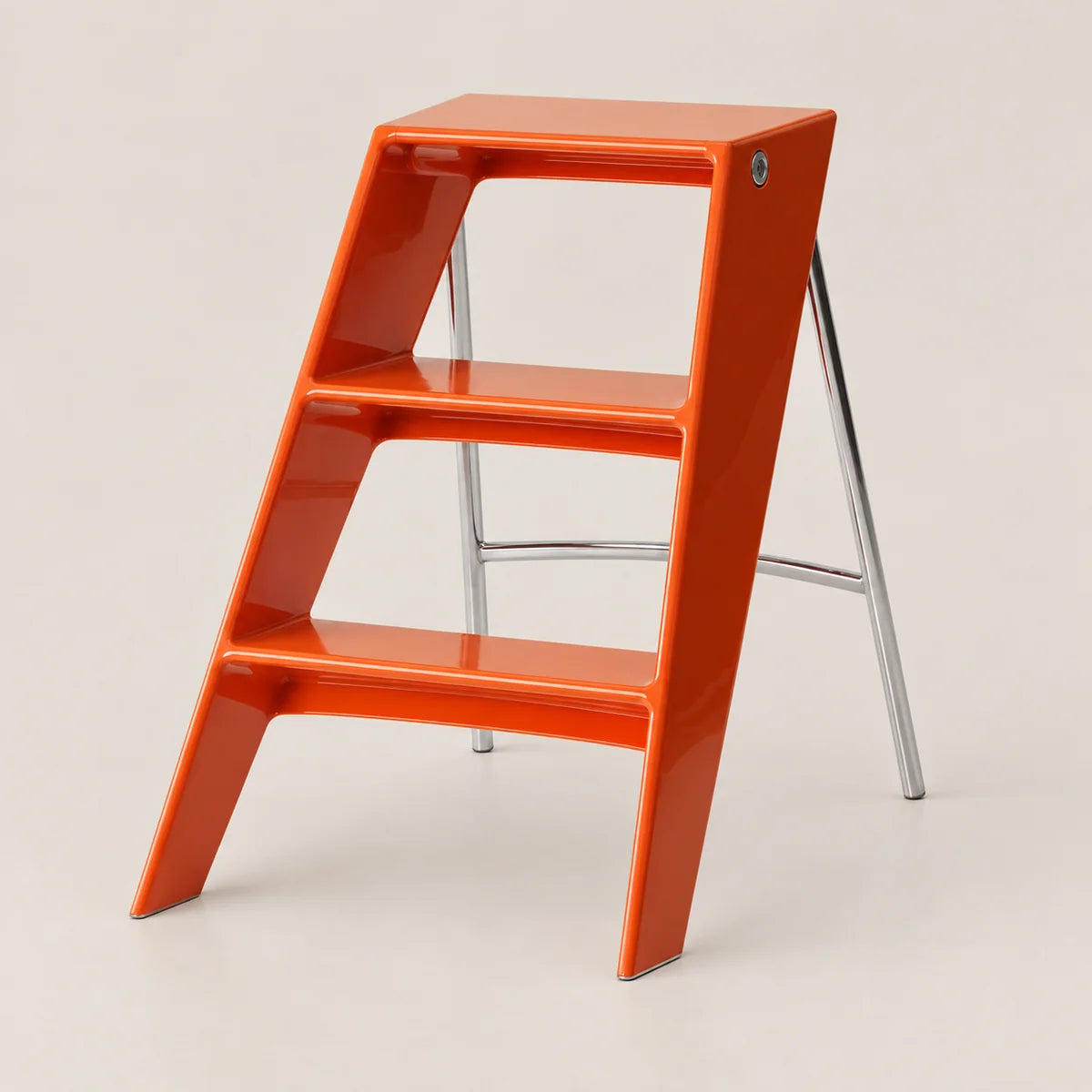 A glossy orange step ladder stool with three steps and a chrome metal support frame, shown on a light beige studio background.