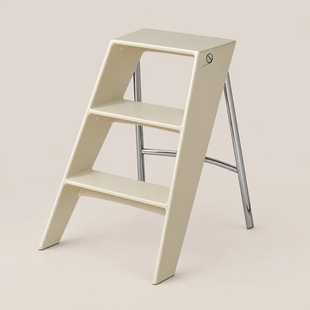A minimalist two-step ladder stool in a warm cream color with a polished silver metal frame, shown on a solid light beige background.