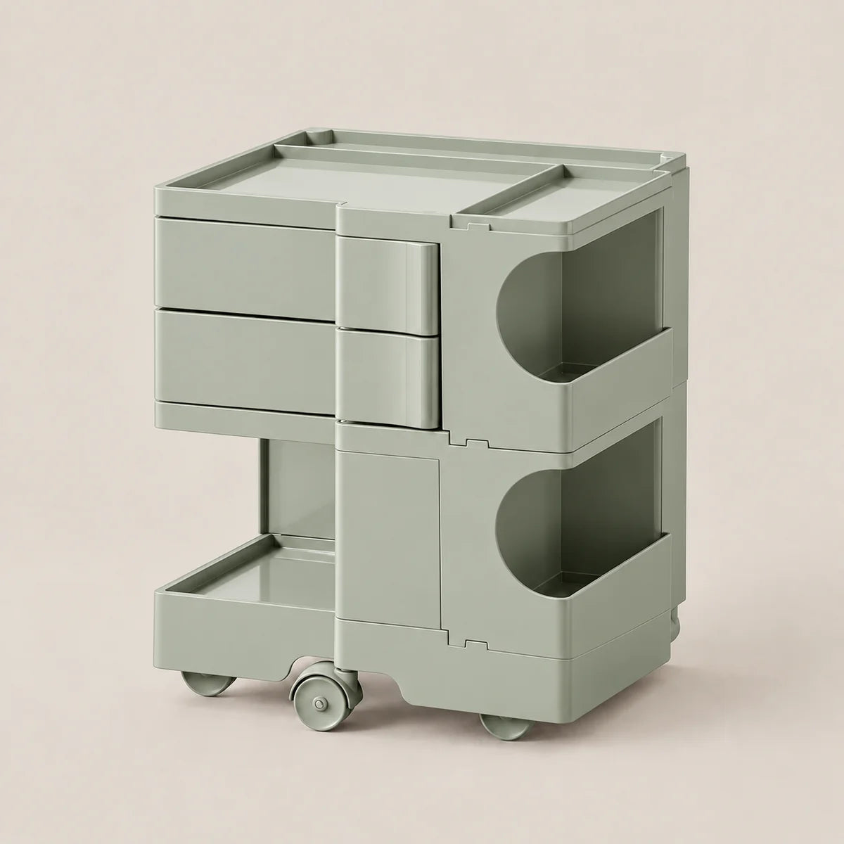 A sage green modular rolling storage cart with three drawers, two open shelves, and caster wheels, shown on a solid light beige background.