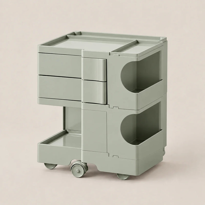 A sage green modular rolling storage cart with three drawers, two open shelves, and caster wheels, shown on a solid light beige background.
