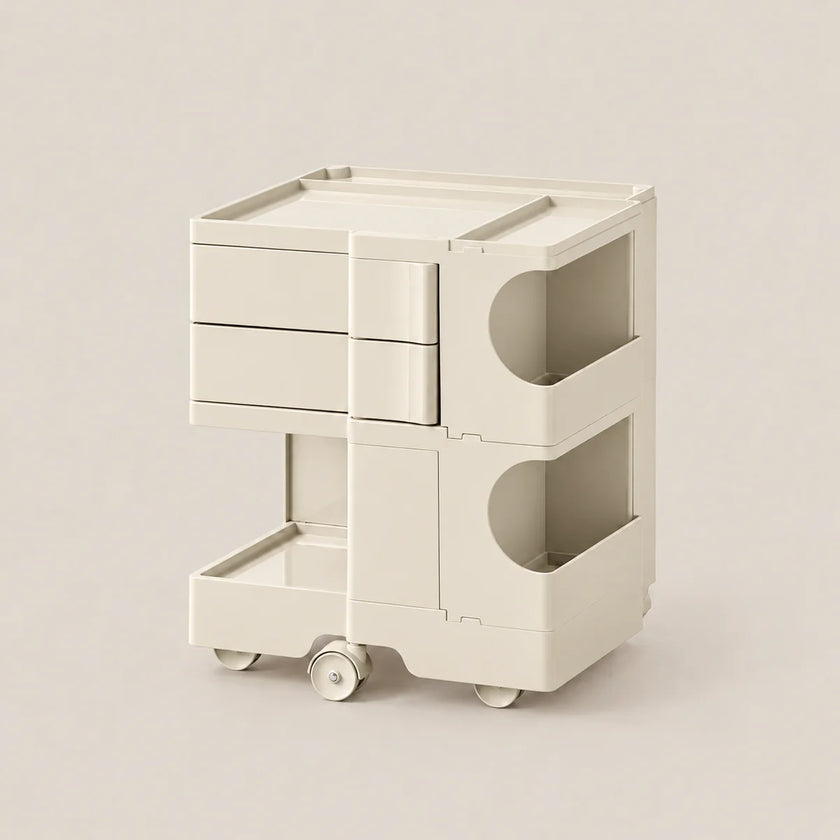 A modern, minimalist two-tier storage cart in a warm off-white/cream color, featuring three drawers on the top tier, open storage compartments with curved cutouts on the side, and a bottom pull-out drawer on wheels, set against a solid light beige background.