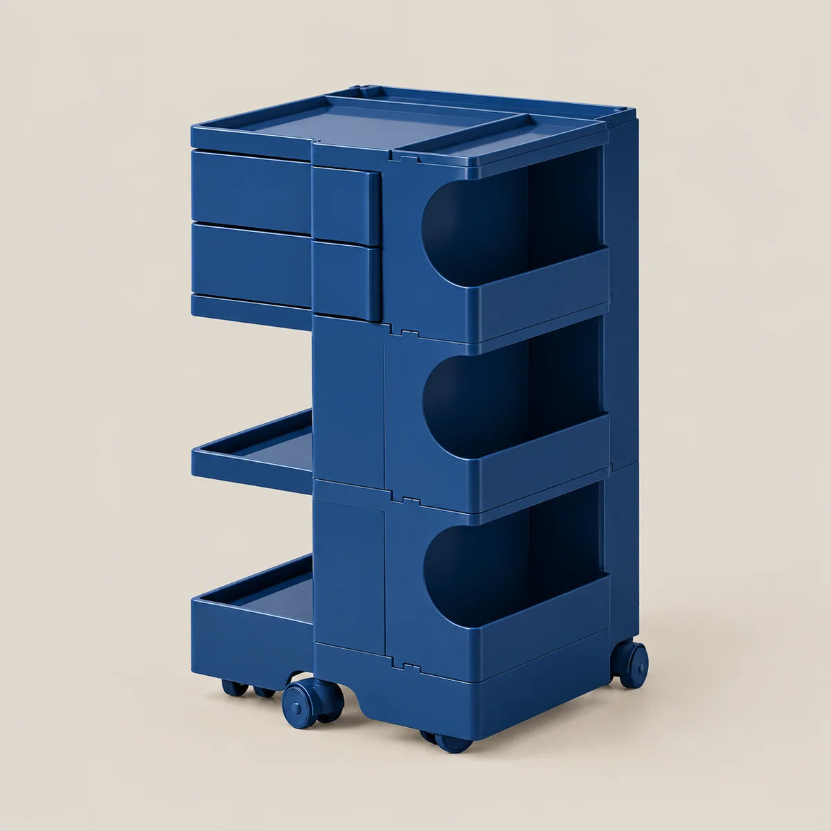 A blue rolling storage cart with three drawers, open shelves, and caster wheels, shown on a plain warm beige background.