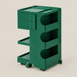 A dark green plastic rolling storage cart with three drawers, three open shelves, and caster wheels, shown on a solid light beige background.