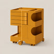 A mustard yellow modular rolling storage cart with three drawers on the left, two open side compartments with semicircular cutouts on the right, and a lower pull-out tray, shown on a light beige background.