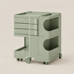 A sage green rolling storage cart with multiple drawers, open storage compartments, and caster wheels, shown on a plain beige background.
