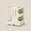 A minimalist, multi-tier plastic storage cart in a warm cream color, featuring three drawers on the top level, two open storage compartments with circular cutouts on the middle and bottom levels, and a pull-out tray on the lower tier. The cart is shown on a clean, solid, light beige background.