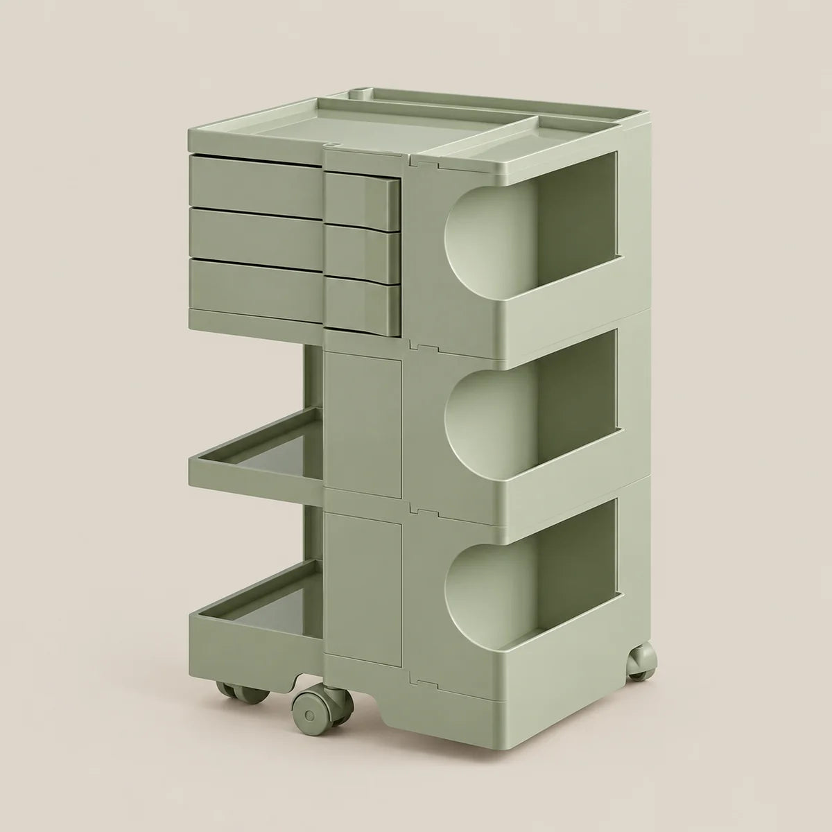 A modern three-tier rolling storage cart in a muted sage green color, featuring three drawers on the top left, two open shelves with circular cutouts, and two caster wheels at the base, set against a solid light beige background.