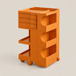 An orange rolling utility cart with three drawers on the left, two open storage compartments on the right, and caster wheels at the base, shown on a plain light beige studio background.