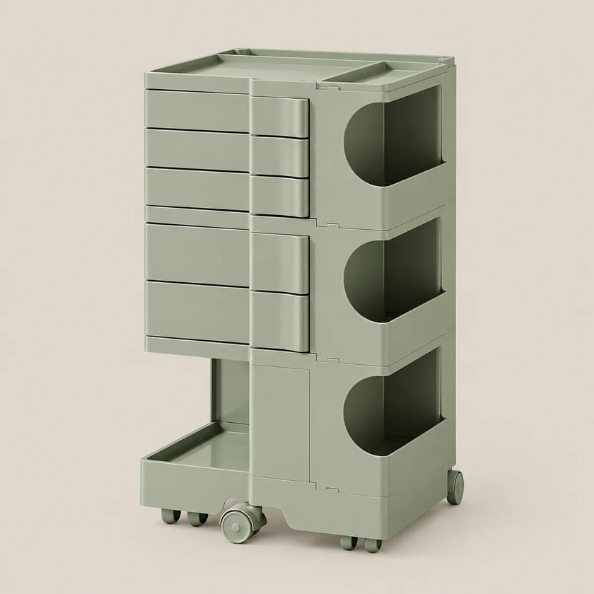 A modern rolling storage cart in a muted sage green color, featuring five drawers on the left, three open storage compartments with circular cutouts on the right, and a lower pull-out tray on casters, set against a solid light beige background.