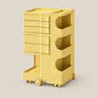 A yellow rolling storage cart with multiple drawers and open storage compartments, shown on a plain light beige studio background.