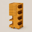 A mustard yellow modular rolling storage cart with multiple drawers, open shelves, and wheels, shown on a solid light beige background.