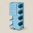 A light blue modular plastic storage cart with multiple drawers, open shelves, and wheels, shown on a solid beige background.