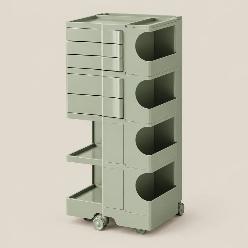 A tall, modular storage cart in a muted sage green color, featuring multiple drawers, open shelves, and wheels, set against a solid light beige background.