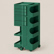 A dark green rolling utility cart with multiple drawers, open storage compartments, and lower pull-out trays, shown on a plain warm beige studio background.