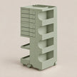 A light sage green rolling storage cart with multiple drawers and open shelves, shown on a plain warm beige studio background.