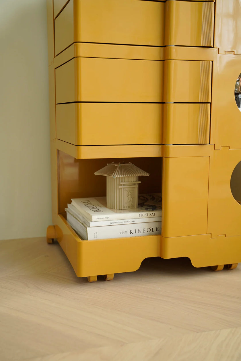 Yellow storage unit with books and a model on a wooden floor.