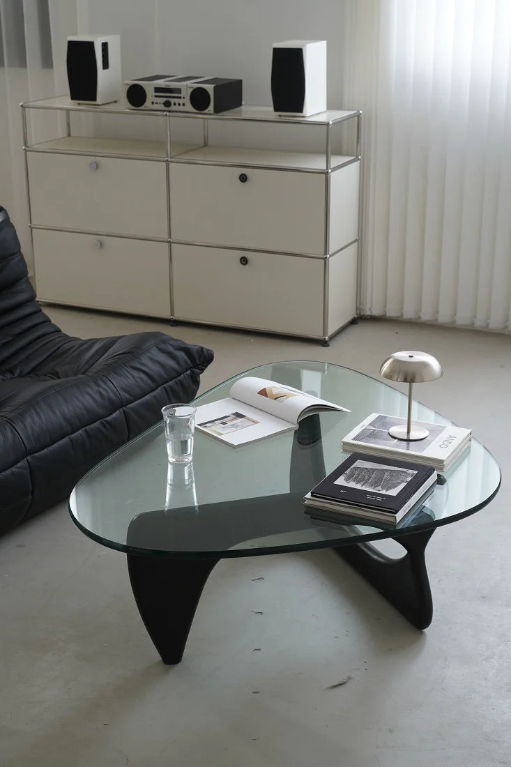 Modern living room with a glass coffee table, black sofa, and white sideboard.