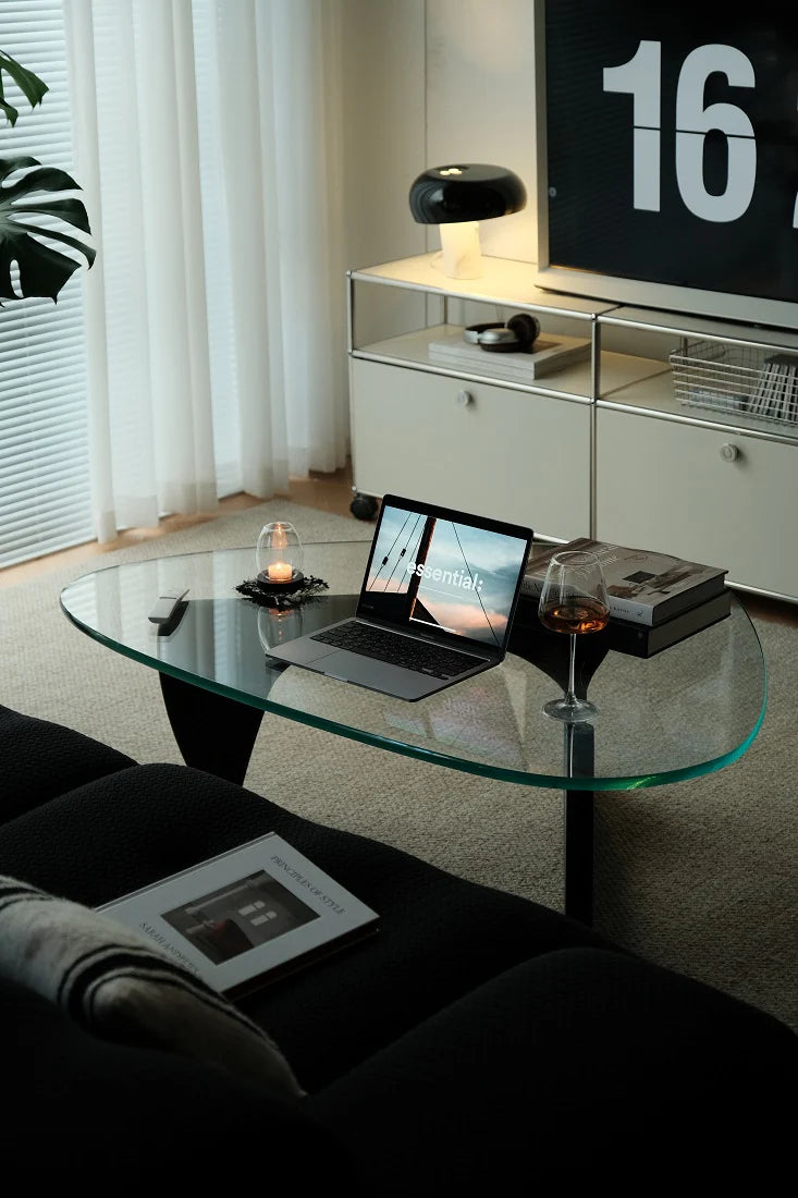 Modern living room with a glass coffee table, laptop, and decorative items.