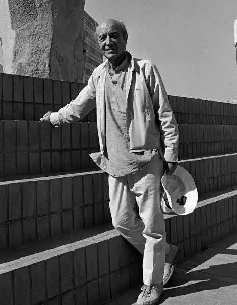 Man standing on a set of stairs wearing a light-colored outfit with a hat.