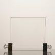Clear glass panel held in place by black clips on a light beige background
