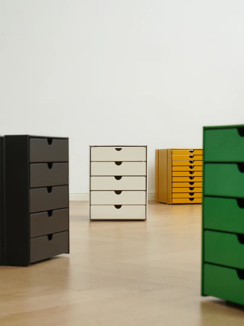 Four drawers in different colors (black, beige, yellow, green) on a light wooden floor.