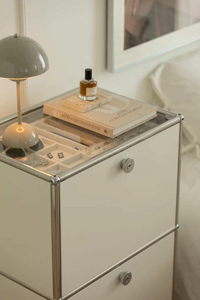 Nighstand with books, lamp, and perfume bottle on a neutral background