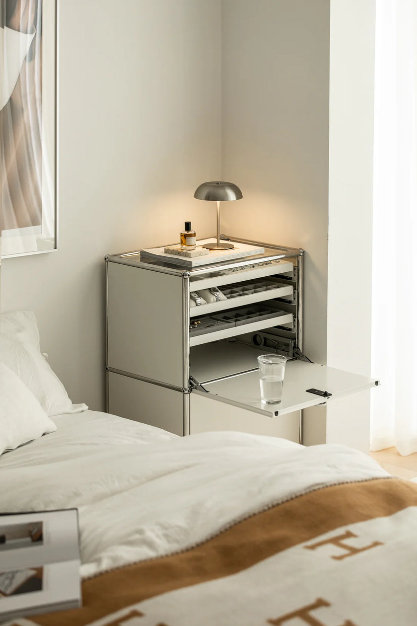 Modern nightstand with lamp and glass next to a bed in a bedroom.
