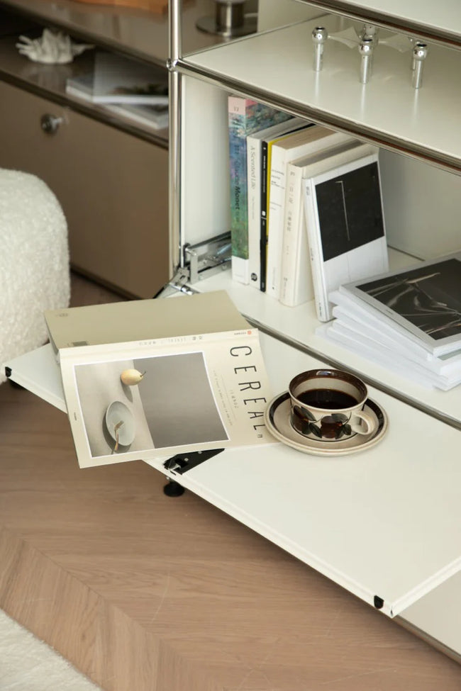 Open cabinet revealing a coffee cup and books on a wooden floor.
