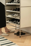 Shoe rack with various shoes on a wooden floor, person wearing slippers nearby.