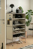Shoe rack with various shoes in a room with plants and a lamp.