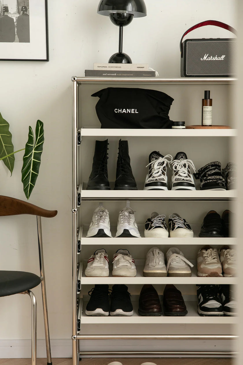 Shoe rack with various shoes, a Chanel bag, and a Marshall speaker against a white wall.