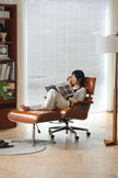 Woman reading a magazine in a modern chair with a bookshelf and lamp in the background