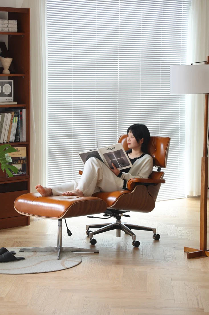 Woman reading a magazine in a modern chair with a bookshelf and lamp in the background
