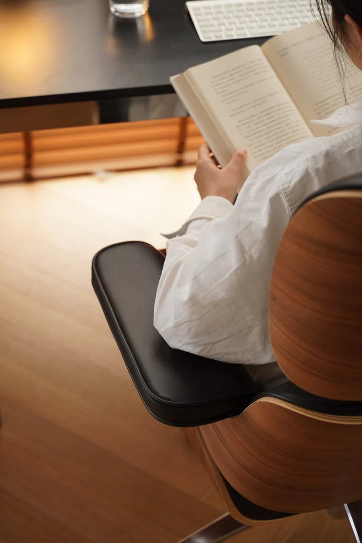 Person reading a book in a chair with a wooden desk in the background