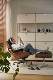 Person relaxing in a modern chair with headphones on, surrounded by minimalistic furniture and decor.