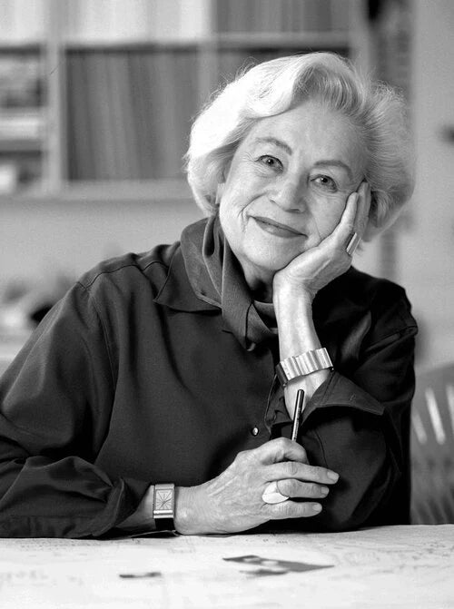 Black and white portrait of a woman sitting at a table with a pen, smiling.