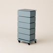 Blue cylindrical storage unit with five drawers on wheels against a beige background
