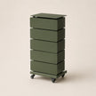 Green cylindrical storage unit with four drawers on a beige background