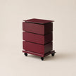 Maroon three-drawer rolling cart on a beige background