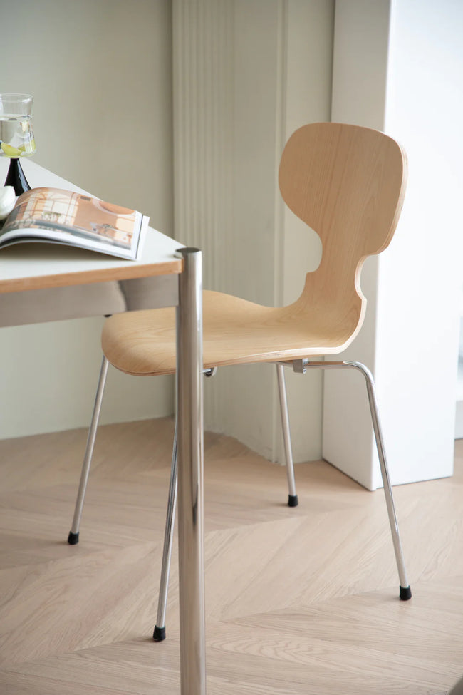 Wooden dining room chair with metal legs next to a table with a magazine on a wooden floor.