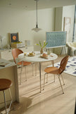 Modern dining area with a modern white round kitchen table and wooden chairs in a well-lit room.
