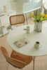 Round white dining table with wooden chairs, a magazine, coffee cup, and vase of flowers in a modern room.