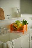 Orange fruit and vegetable plastic storage containers on a kitchen counter with sink and cabinets in the background