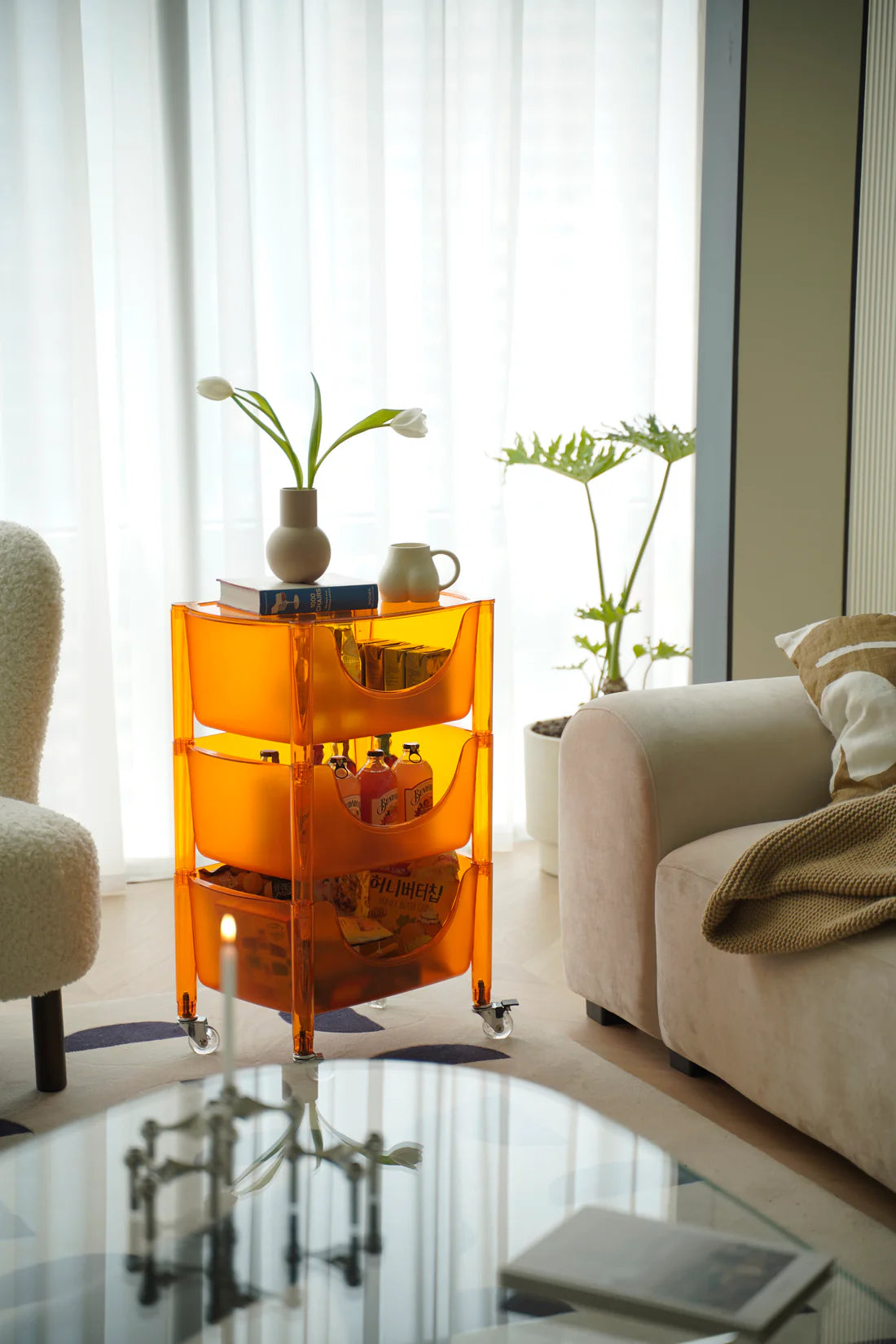 Orange 3 tier rolling cart with decorative items in a living room setting.