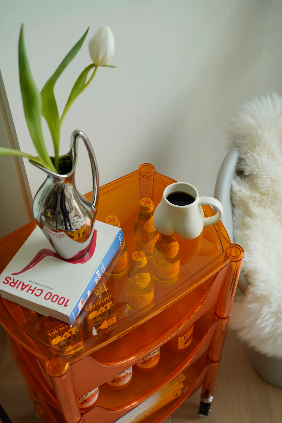 Orange storage containers side table with a book, vase, and coffee cup on a light-colored floor.