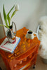 Orange storage containers side table with a book, vase, and coffee cup on a light-colored floor.