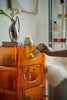 Lady holding a can of beer next to an orange 3 tier rolling cart with bottles on a shelf.