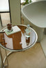 Small round side table with a bottle and glass on a reflective surface, with a blurred background.